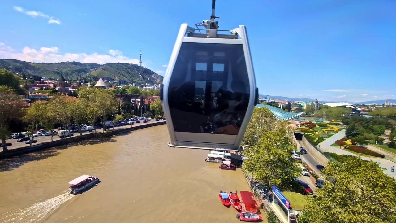 Funivia che passa sopra il fiume con barche e traffico nel centro di Tbilisi in una giornata di sole