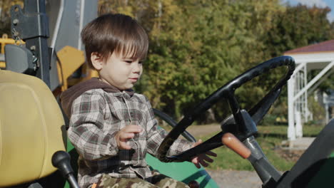 The-boy-enthusiastically-plays-tractor-driver.-Sits-behind-the-wheel-of-an-old-tractor-on-the-farm