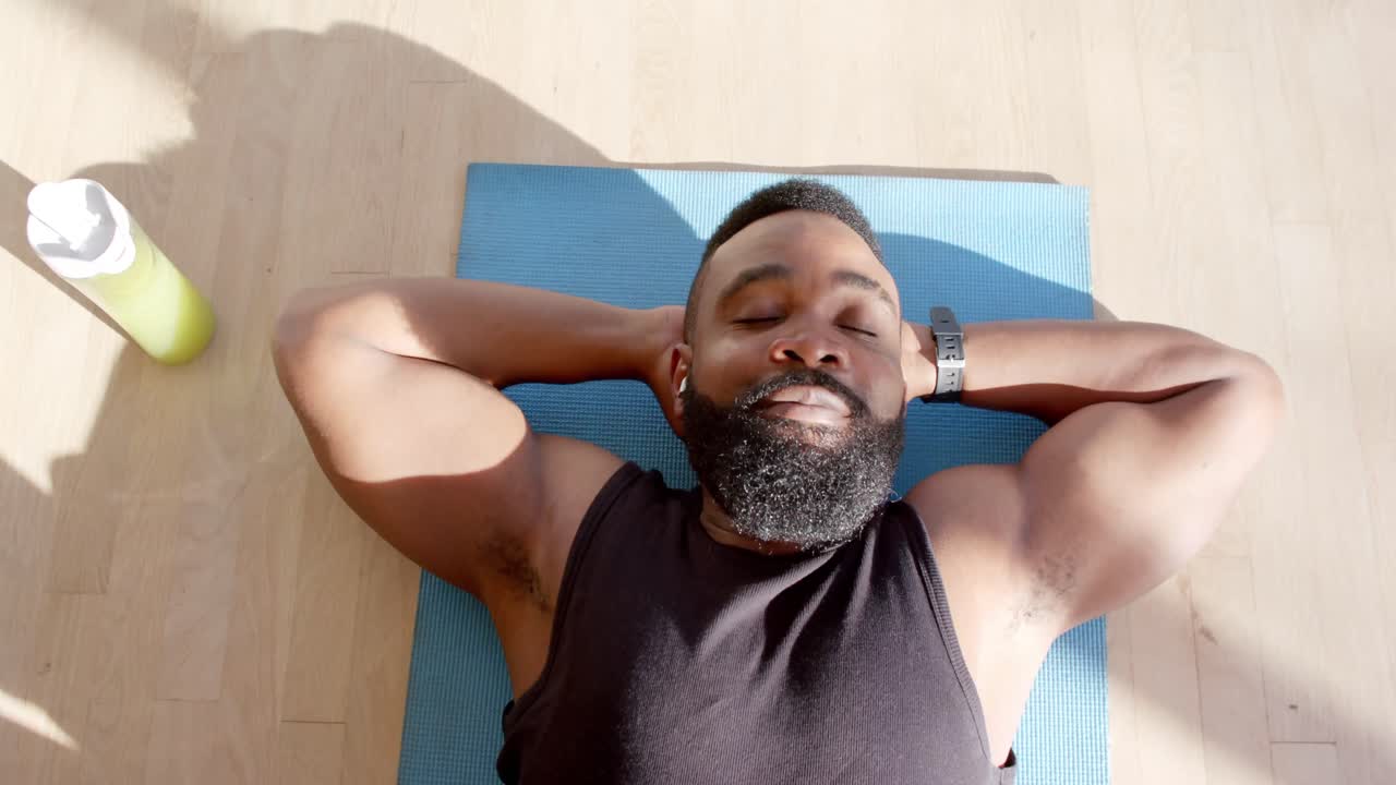 Happy african american man resting on mat at sunny home, slow motion