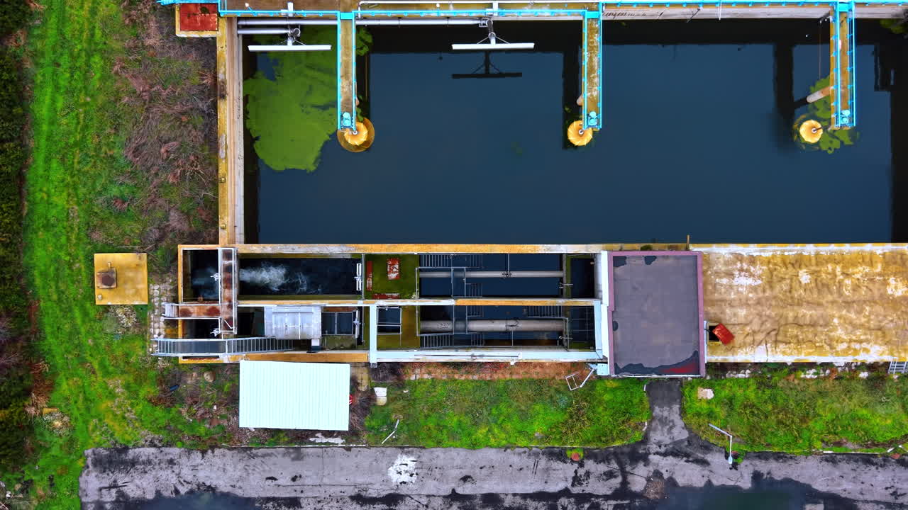Top down close up of wastewater treatment machinery. Vertical aerial shot of rectangular tanks with water, pipes, and green algae during the purification process