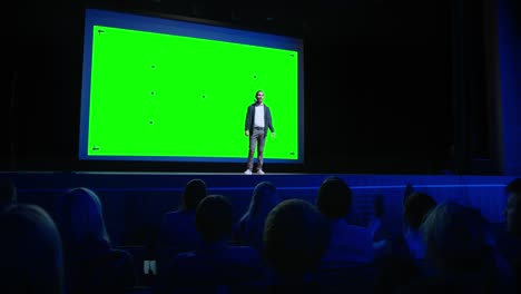 keynote speaker presents new product to the audience, behind him movie theater with green screen, mock-up, chroma key. business live event or device reveal