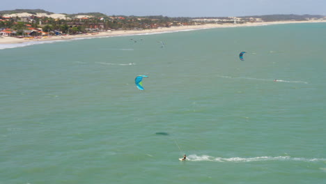 Vista-Aérea-De-Personas-Practicando-Kitesurf-Y-Un-Pequeño-Pueblo-Alrededor,-Cumbuco,-Ceará,-Brasil.