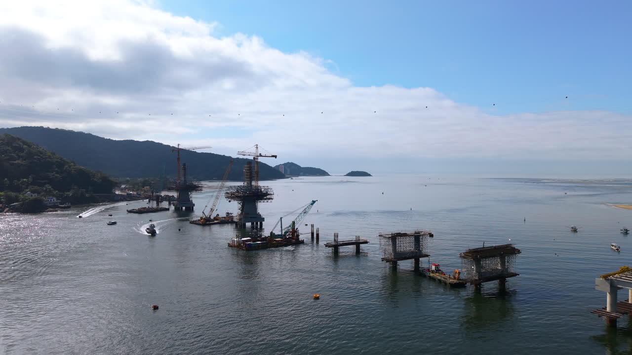 Panning panoramic drone movement near the new Guaratuba-Matinhos Bridge with construction barges and machinery, Paraná, Brazil