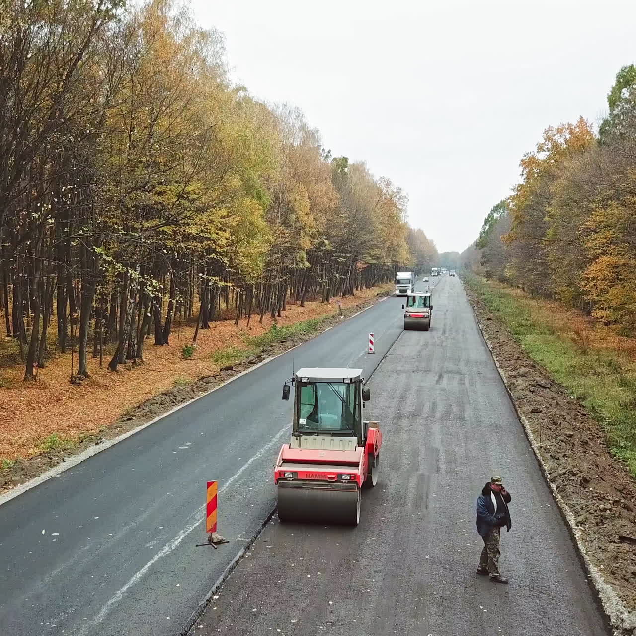 Heavy equipment while building an asphalt road. Steamroller pressing new asphalt in highway in autumn. Road works on natural background.