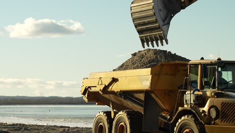 excavator loading industrial dump truck at beach building site, slow motion