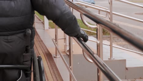 a person with a disability moves along the street in a wheelchair, climbs the ramp