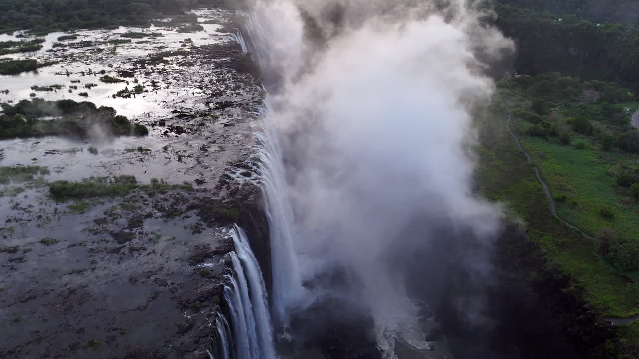 Aerial view of Victoria Falls with powerful waterfall plunging into gorge, mist rising above lush green forest, dramatic natural wonder and iconic travel destination in Africa
