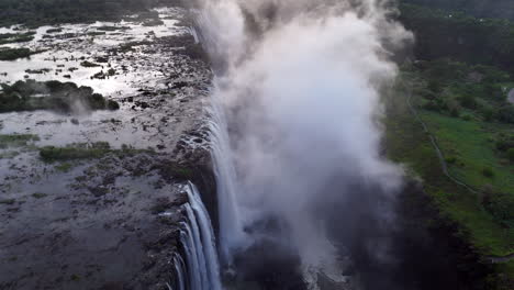 aerial view of victoria falls with powerful waterfall plunging into gorge, mist rising above lush green forest, dramatic natural wonder and iconic travel destination in africa