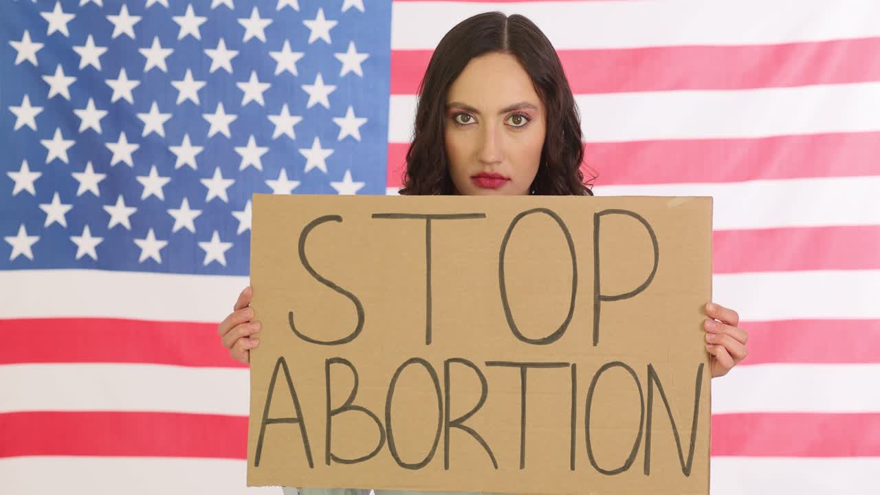 Woman holds stop abortion sign against american flag in studio