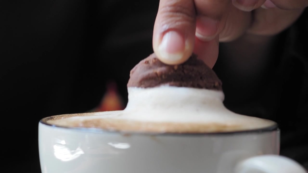 Persona che intinge un biscotto al cioccolato in una tazza di cappuccino