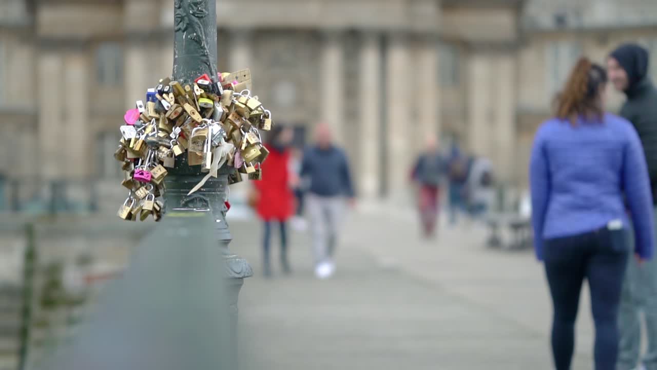 Clip of love locks on a pole in paris city centre with people walking out of focus blur in the background