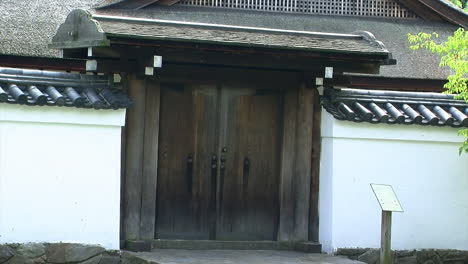 close-up of the roofed hinoki wood entrance gate and tiled wall of a japanese house