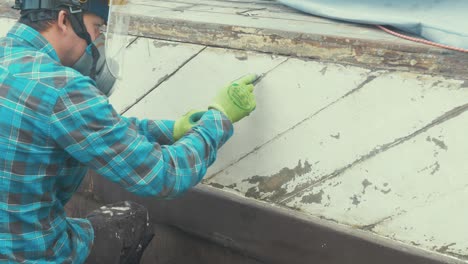 young man using a reefing hook to clean boat plank seams