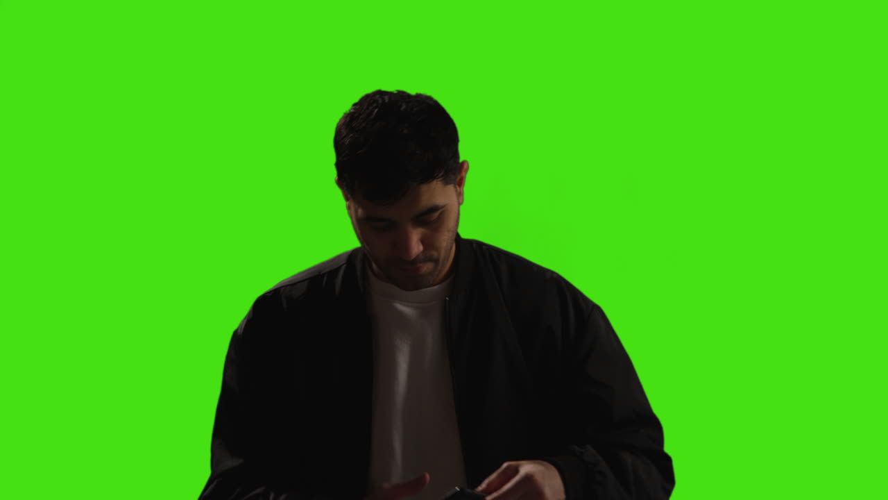 joven respondiendo a una llamada en el teléfono móvil de pie contra el fondo del estudio de pantalla verde con iluminación de bajo nivel 1