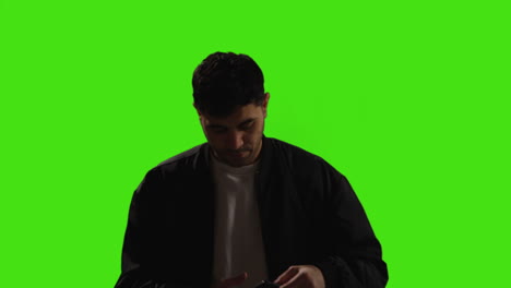 Young-Man-Answering-Call-On-Mobile-Phone-Standing-Against-Green-Screen-Studio-Background-With-Low-Key-Lighting-1