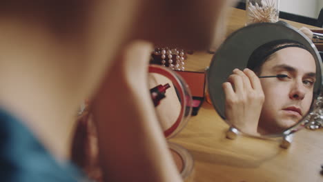 transgender man looking in table mirror and applying mascara