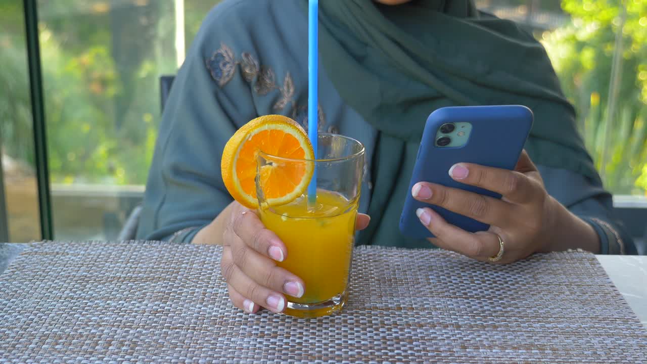 mujer disfrutando de jugo de naranja y usando el teléfono en un café