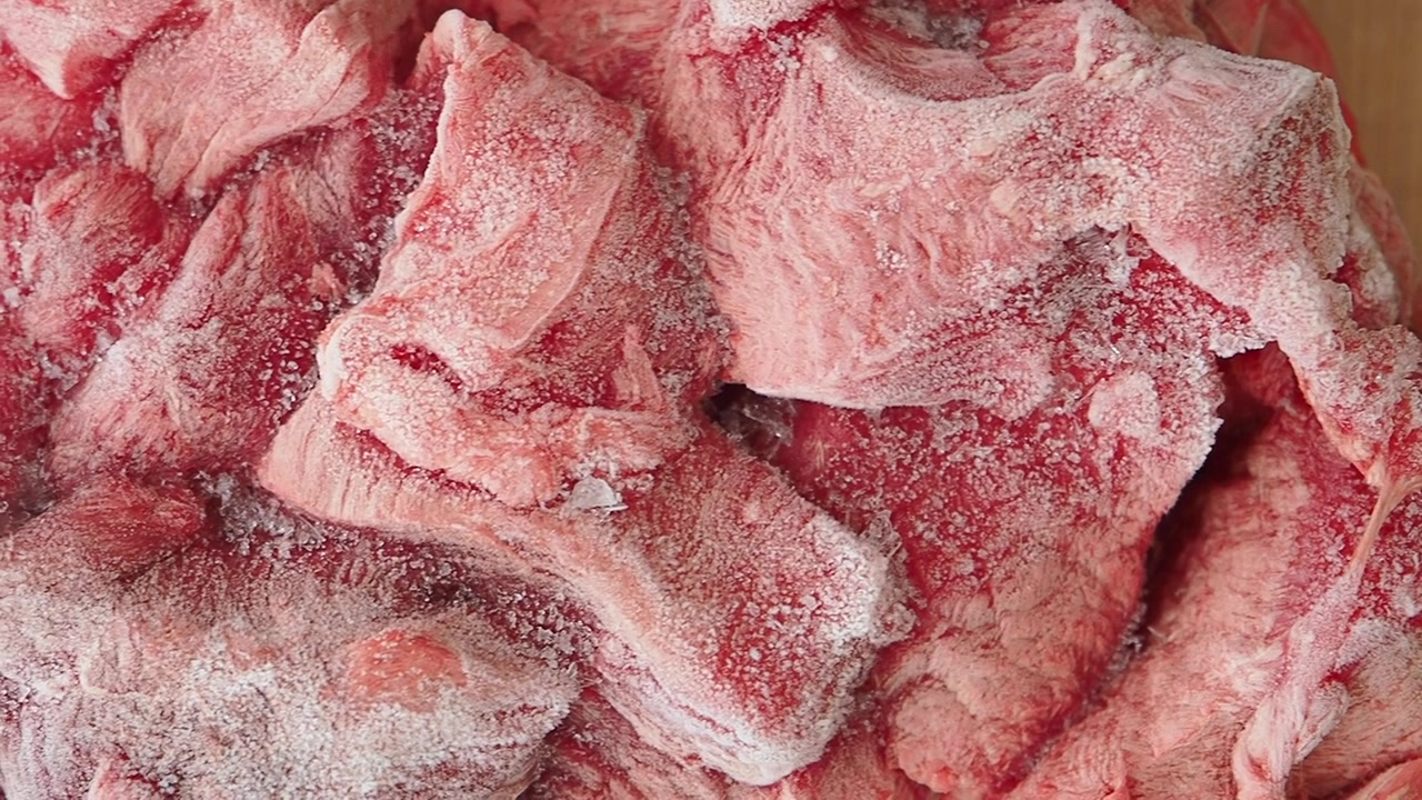 Primo piano di pezzi di manzo crudo congelato su un tagliere di legno