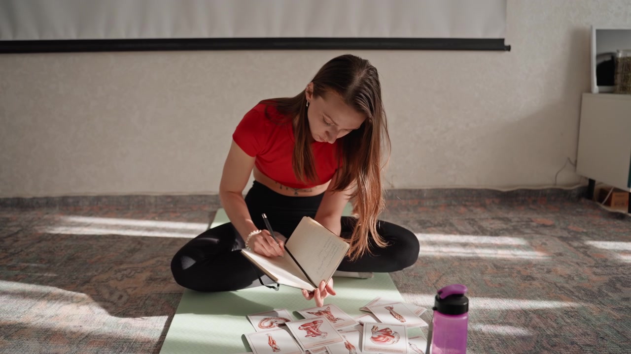 Una persona se prepara para una sesión de ejercicio en casa. Una mujer organiza tarjetas de fitness y páginas de diario en la alfombra, configurando su rutina de ejercicios en un acogedor espacio hogareño.