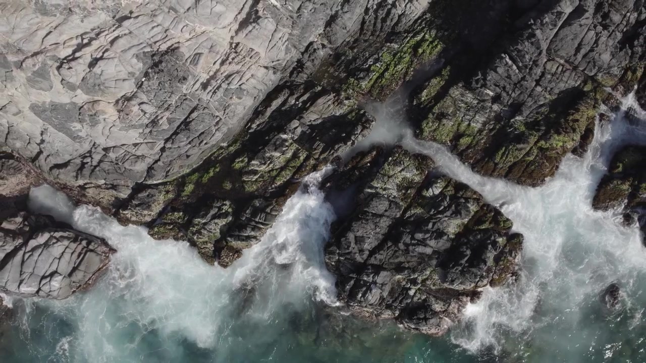 Drammatica prospettiva dall'alto di potenti onde marine che si infrangono su rocce scure e affilate, evidenziando l'energia grezza e l'erosione della costa. 4K Dlog.