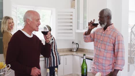 Diverse-senior-couples-drinking-wine-and-preparing-vegetable-salad-in-a-kitchen