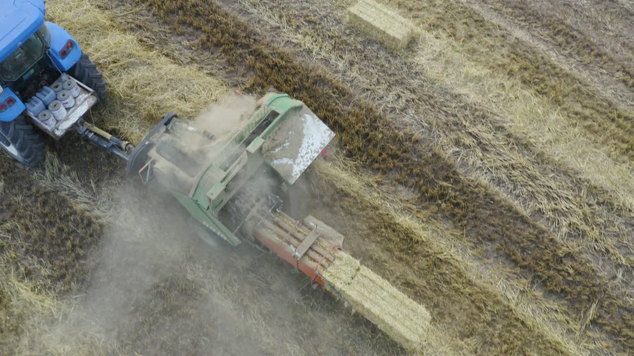una vista aérea de un granjero en un tractor con un remolque lleno de balas de paja.