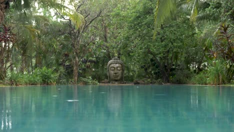 a buddha head statue surrounded by green trees and water, tranquility in the rain