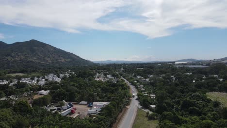 Panning-to-the-left-showing-a-small-town-nestled-in-the-foothills-of-a-mountain-with-abundant-vegetation-and-a-little-traveled-road-in-the-foreground