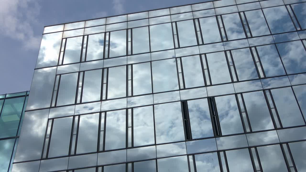 lapso de tiempo de un cielo azul de verano con nubes que se reflejan en la fachada de vidrio de un edificio de oficinas