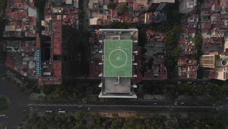 Vista-Aérea-De-Pájaros-Vista-De-Arriba-Hacia-Abajo-Del-Edificio-De-Oficinas-Alto-Con-Helipuerto-Verde-En-La-Parte-Superior-Y-El-área-Circundante.-Cámara-Alejándose.-Ciudad-De-México,-México.