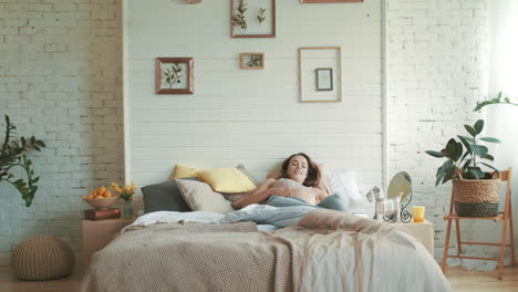 mulher grávida sorridente deitada na cama em casa. mãe de barriga relaxando no quarto da manhã.