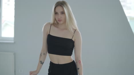 chica en forma con ropa negra actuando contemporáneamente. bailarina muestra movimientos fluidos, cuerpo y manos ondas en la habitación blanca. coreografía de danza de ballet moderno. joven se mueve suavemente