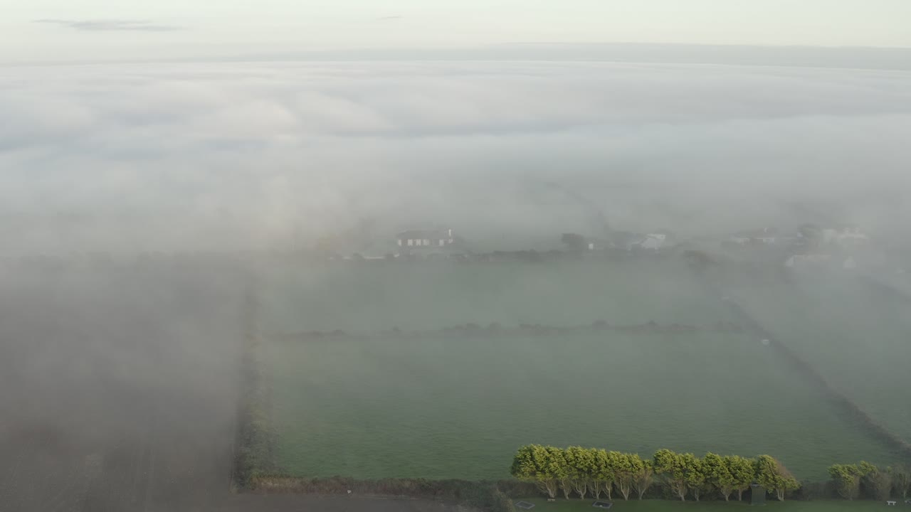 Aerial: Coastal fog rolls over bucolic green farmland on misty morning