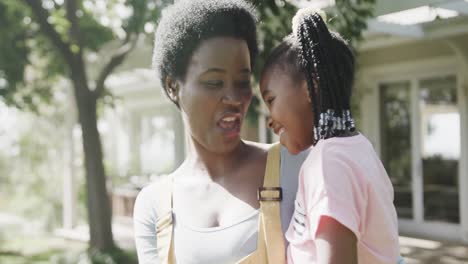 portrait of happy african american mother holding daughter in sunny garden, slow motion