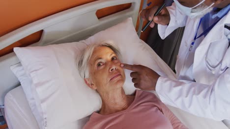 african american male doctor using penlight examining eye of senior caucasian female patient