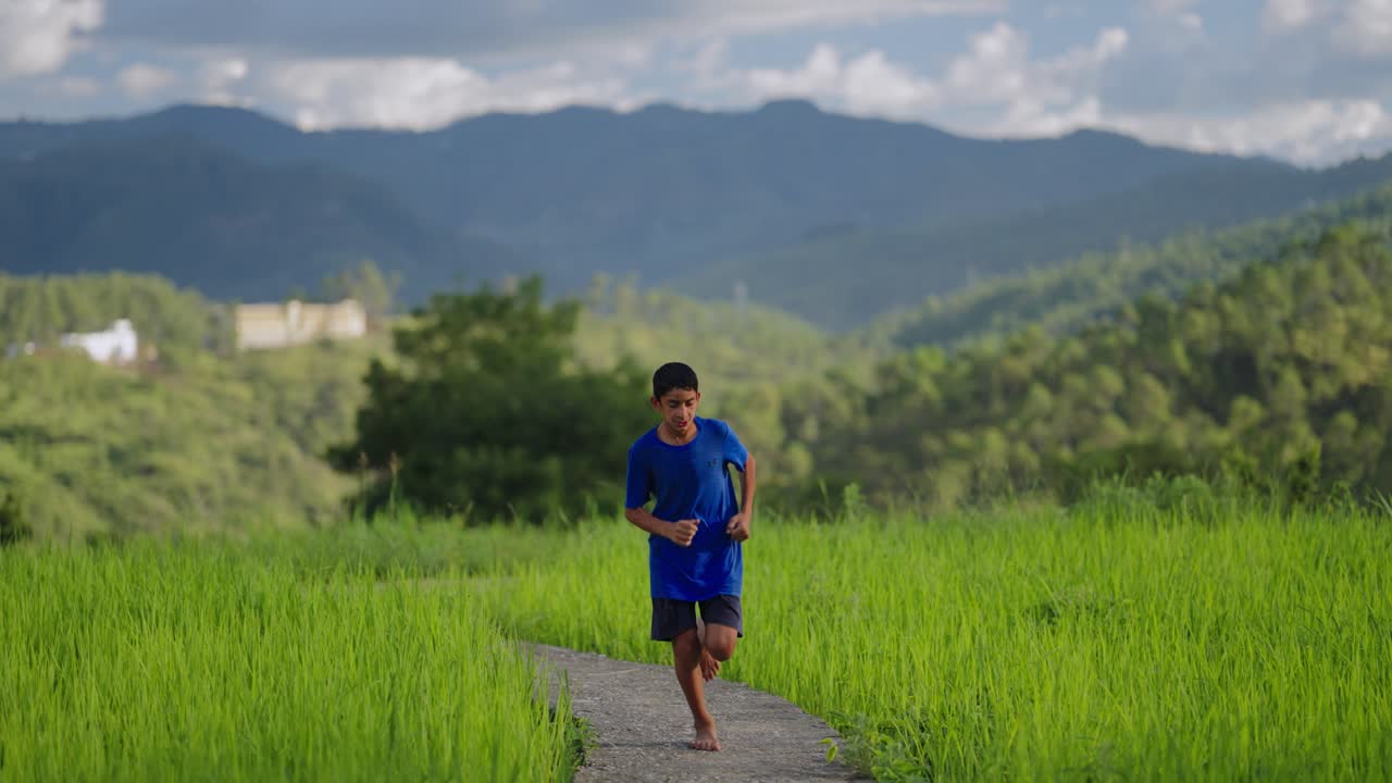 Young Indian child sprinting through green rice fields with bare feet and blue shirt, carefree village life, 4k video