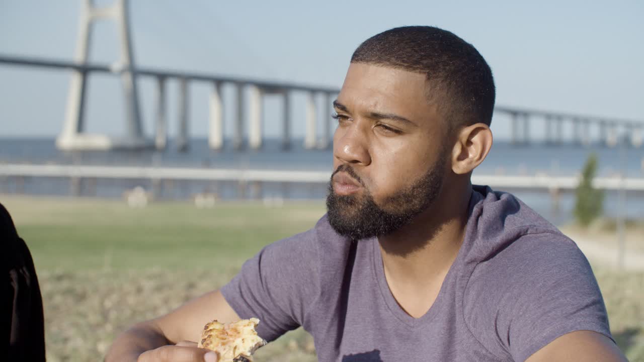 un hombre afroamericano guapo sonriente comiendo pizza.