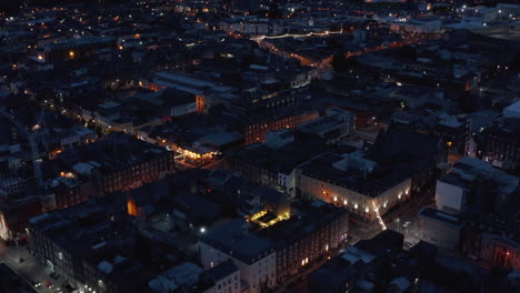 Fly-above-urban-neighbourhood-at-night.-Aerial-view-of-buildings-and-streets-lit-by-lights.-Limerick,-Ireland