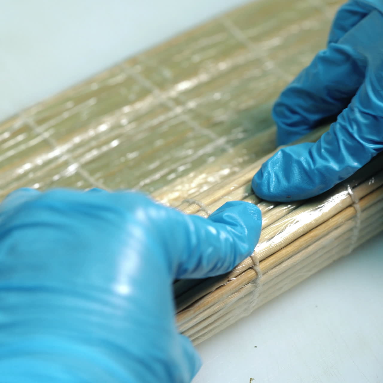 Close-up of professional chef's hands rolling a sushi roll on seaweed mat Sqare video