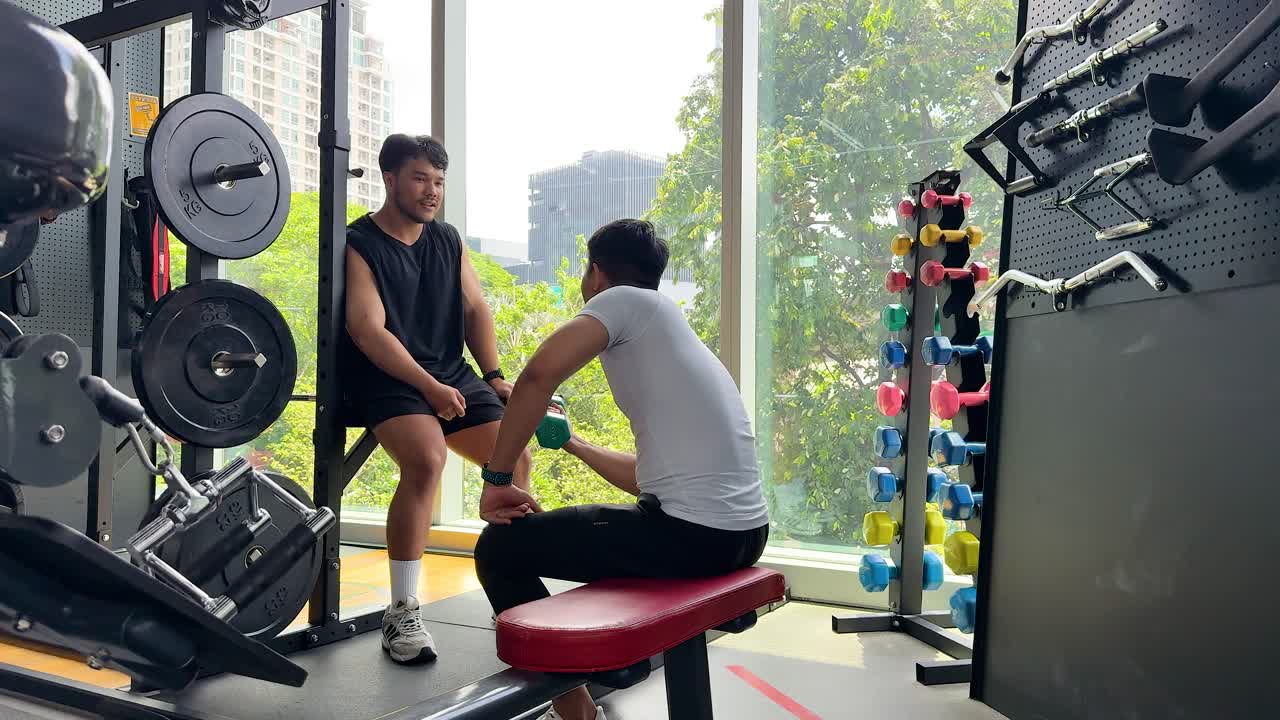 Two people talking during a workout in a bright, modern gym with fitness equipment