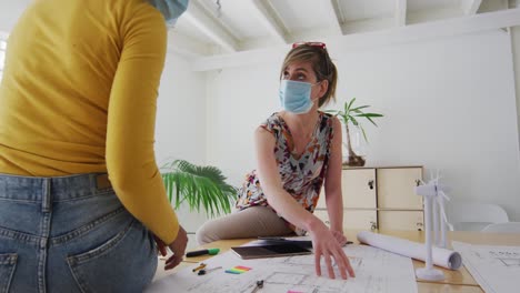 two woman wearing face mask discussing over documents on table at office