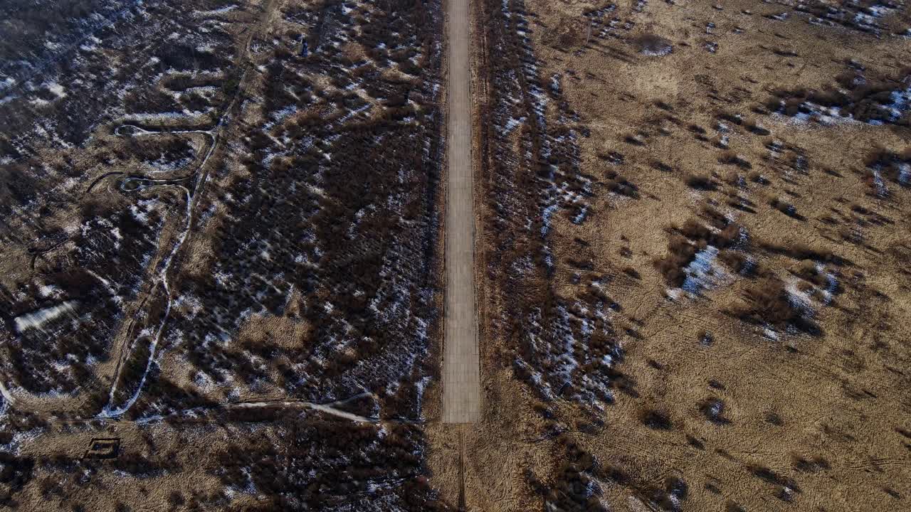 Drone captures remote airfield runway cutting through barren spring landscape 4K