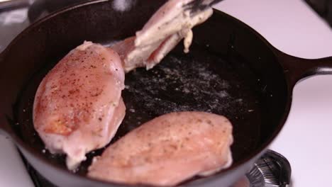 pre frying three pieces of filled chicken breasts on top of gas stove in the forged frying pan