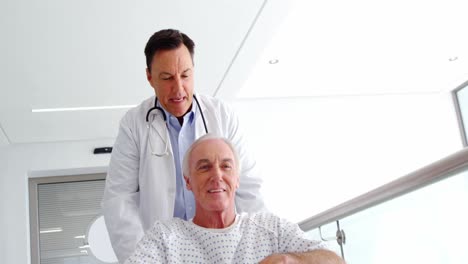 médico sosteniendo a un paciente mayor en silla de ruedas en el pasillo