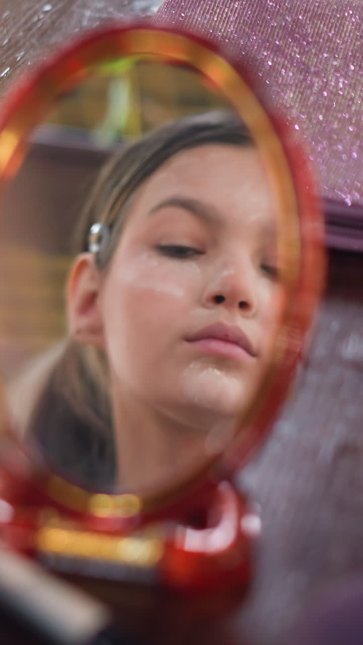 Adolescente mirándose al espejo y aplicándose polvos con una esponja suave, mirada contemplativa y fondo de tocador brillante, primer plano mostrando iluminación y difuminado, iluminación artística y ambiente tranquilo