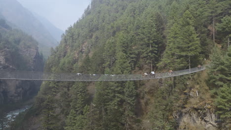 drone shot of mules crossing hillary bridge on everest trekking trail, surrounded by hills and dense forest under midday sunlight landscape look serene at mount everest region of nepal