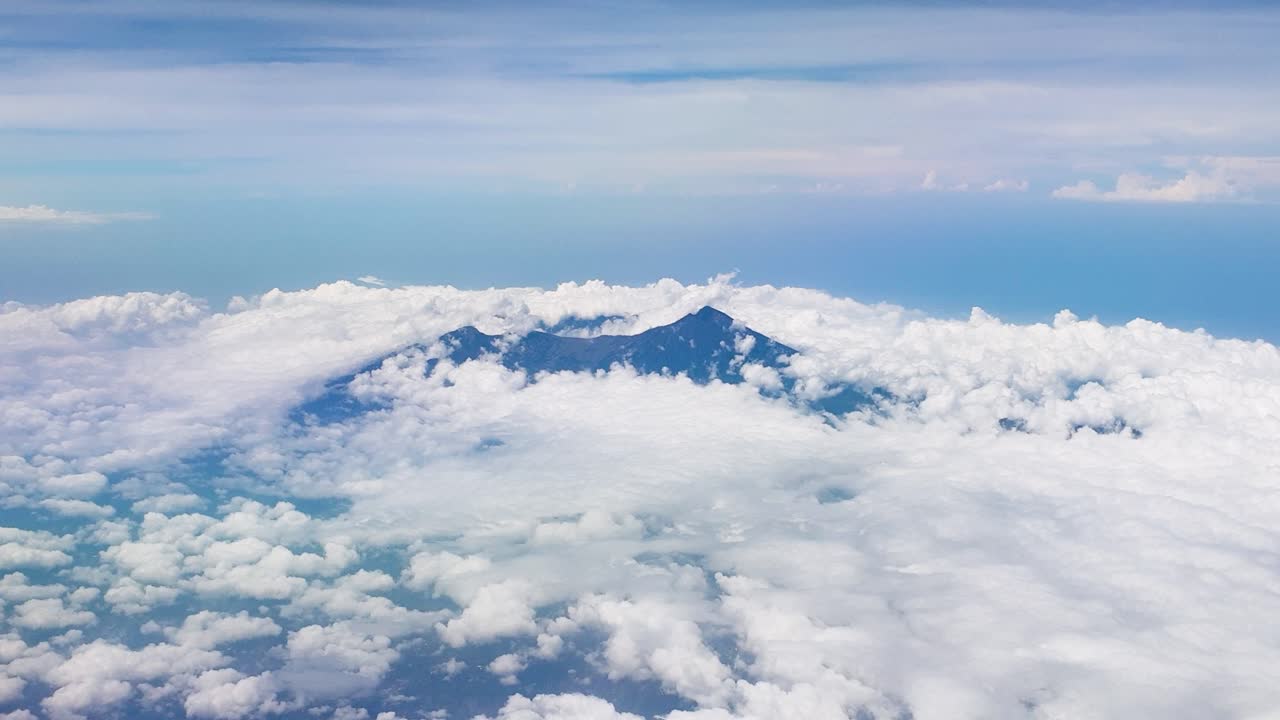 인도네시아에서 두꺼운 구름을 가로질러 아오르는 거칠고 바위가 많은 화산 꼭대기의 공중 사진