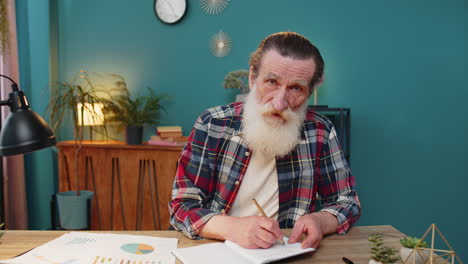 pov shot of senior man looking to camera listening to colleague talking writing down notes on diary
