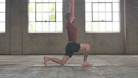 man in an industrial warehouse practicing yoga, the pose of low lunge with side stretches.