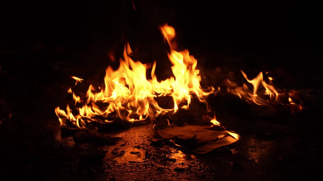 Bright orange and yellow flames spreading across a dark ground, creating a burning inferno with sparks and embers, symbolizing danger, destruction, warmth, and the power of fire